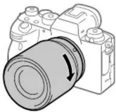 SONY Alpha A9 II - Enquanto empurra a objetiva ligeiramente em direção da-camera, rode a objetiva lentamente na direção da seta até fazer clique na posicao bloqueada. - 1