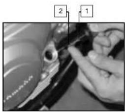 Close-up photo of a hand holding a mechanical component with numbered annotations pointing to parts 1 and 2.