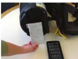 Hand holding a white card next to a black electronic device with yellow cables, likely part of a device or app interface.