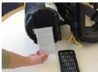 Hand holding a white card next to a black electronic device and a calculator on a table