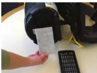 Hand holding a card with visible text, next to a black electronic device and a calculator on a table.