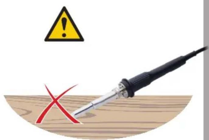 Safety warning symbol with a soldering iron and red X mark on wooden surface