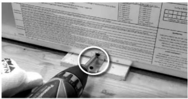 Black-and-white photo showing a hand using a power tool to adjust or install a mechanical component, with a magnified inset highlighting the component's detail.