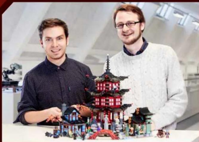 Two men posing with a detailed LEGO model of a traditional Japanese pagoda in an indoor setting (no visible text or symbols)