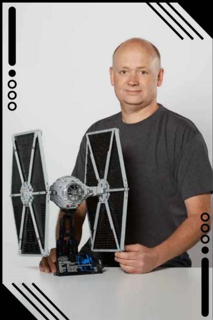 Portrait of a man holding a model of a Star Wars II satellite with extended solar panels (no visible text or symbols)