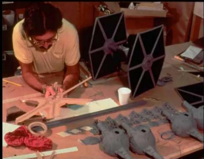 A craftsman working on a handmade model of a starry structure at a workshop, surrounded by fabric and materials (no visible text or symbols)