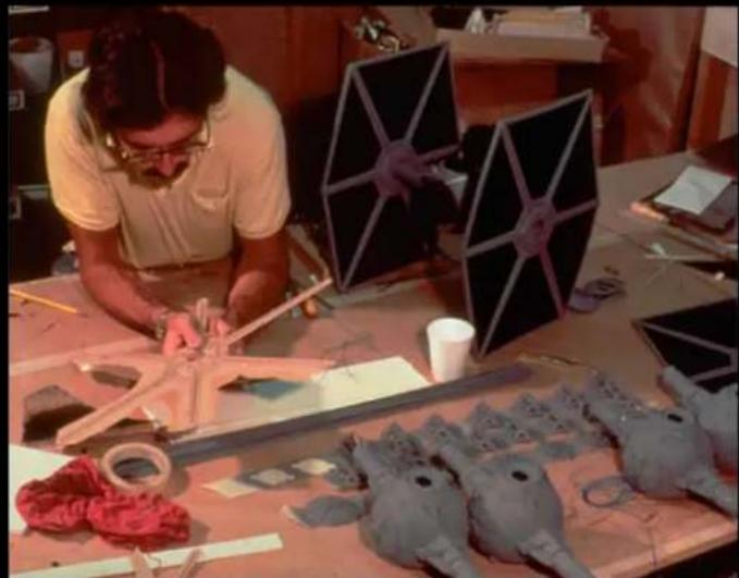 A craftsman working on a handmade textile project with multiple star-shaped fabric pieces and red fabric, surrounded by finished materials (no visible text or symbols).