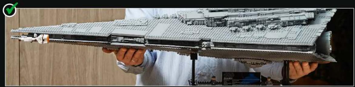 Person holding a detailed LEGO model of a war-torned building, no visible text or symbols on the model itself.