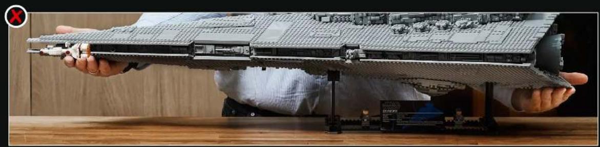 Person holding a detailed LEGO-style warship model on a wooden table (no visible text or symbols)