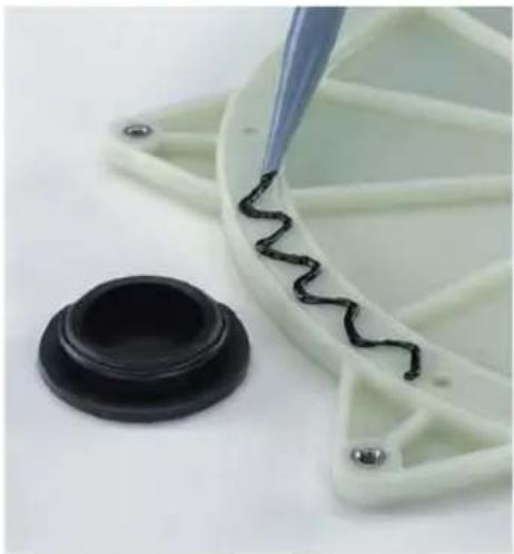 Close-up of a green plastic container with black wavy lines being cut by a tool, alongside a black circular base (no text or symbols visible)