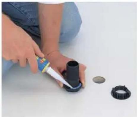 Person using a spray can to apply black plastic components on a white surface, with other small circular parts nearby (no text or symbols visible)
