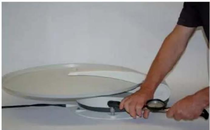Person using a magnifying tool to clean or operate a large circular fan on a white surface (no text or symbols visible)