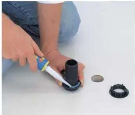 Person using a glue gun to apply black rubber cap onto a surface with other small components nearby (no text or symbols visible)