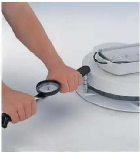 Person using a pressure gauge to measure a white cylindrical device on a white surface (no text or symbols visible)
