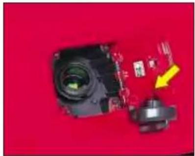 Close-up of a camera module with a yellow arrow pointing to a small electronic component on a red background (no text or symbols visible)