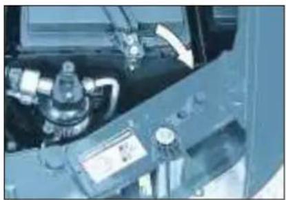 Close-up of a car engine bay with visible components and a white arrow pointing to a component (no text or symbols)
