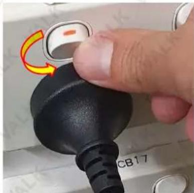 Close-up of a finger pressing a black rubber plug with a yellow curved arrow indicating rotation (no text or symbols visible)