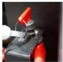 Close-up of hands using a tool to clamp or wire around a metallic object (no visible text or symbols)