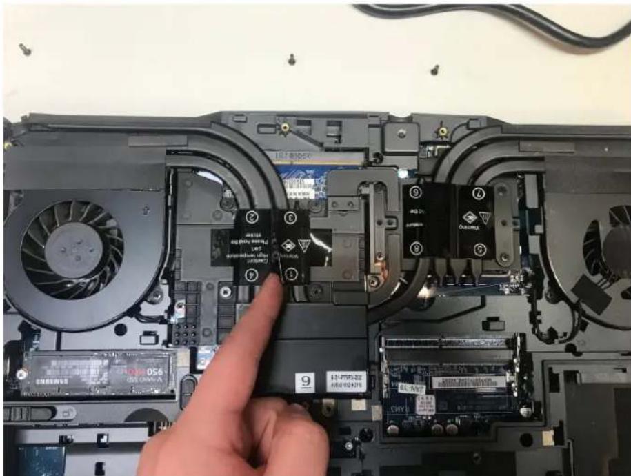 Laptop interior with visible circuit board and labeled components, showing a finger pointing to a component.