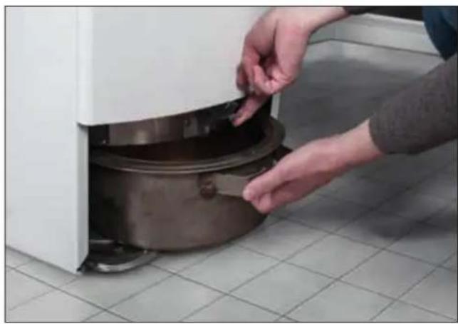 Person placing a small container into a white appliance with tiled floor (no text or symbols visible)