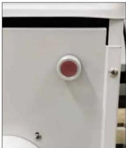 Close-up of a white industrial cabinet with a circular red component and metallic buttons. No visible text or symbols.