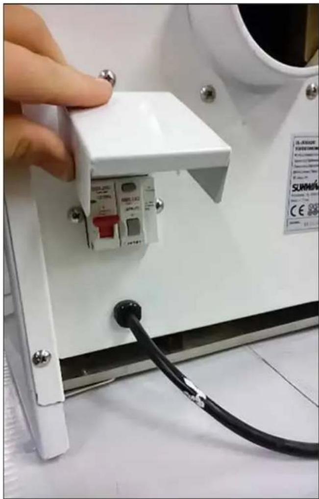 Close-up of a white electronic device with a small circuit breaker and cable inserted, showing a hand interacting with the component (no visible text or symbols)