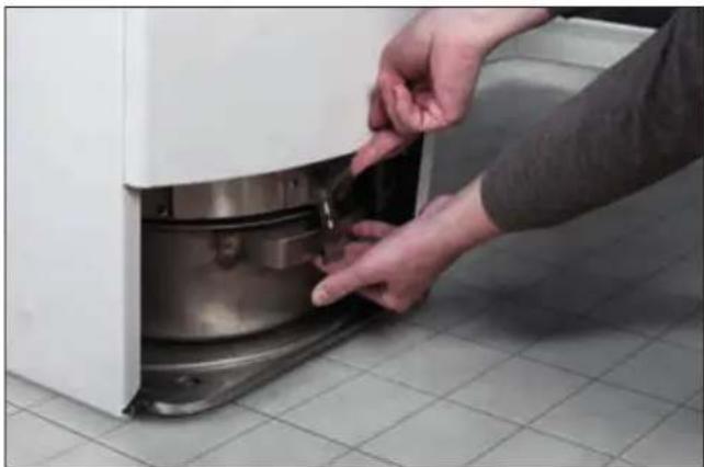 Person installing or adjusting a component on a white appliance, tiled floor background (no visible text or symbols)