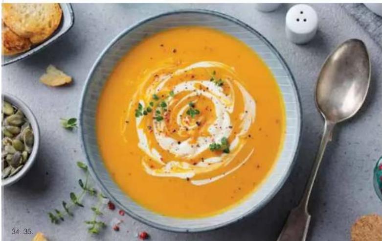 Bowl of creamy orange soup with spiral swirl garnish, accompanied by a spoon and side dishes (no text or symbols visible)