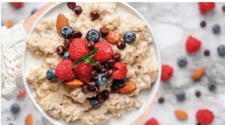 Close-up of a bowl of porridge topped with fresh berries and nuts, surrounded by scattered strawberries and blueberries (no text or symbols visible)