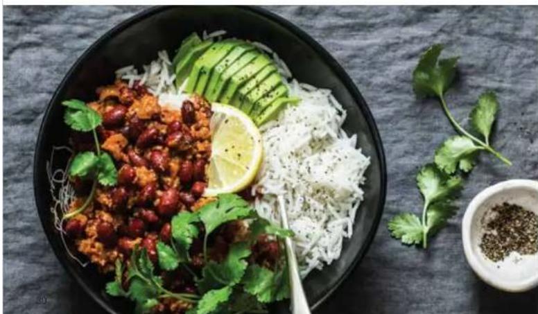 A bowl of spicy rice salad with red beans, shredded white noodles, and garnished with cilantro and a lemon slice (no text or symbols visible)