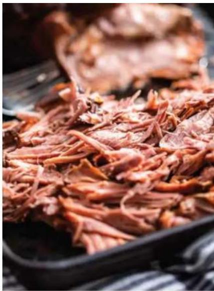 Close-up of cooked meat in a black pan, with blurred background showing meat slices (no text or symbols visible)