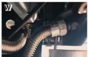 Close-up of a flexible hose with metallic fittings and connectors, mounted on a vehicle (no visible text or symbols)