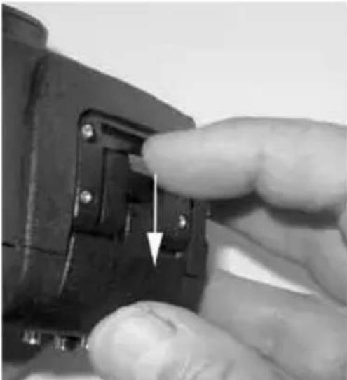 Close-up of a finger pressing a small mechanical component with a white arrow indicating the adjustment (no text or symbols visible)