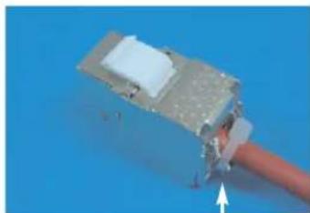 Close-up of a mechanical component with a white block and metallic housing, attached to a thin wire against a blue background (no visible text or symbols)