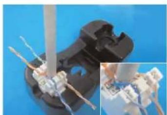 Close-up of a black plastic electrical connector with wires inserted, showing internal components and a magnified inset (no text or symbols visible)