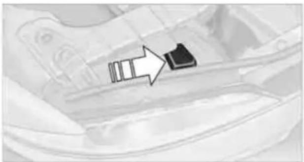 Close-up of a car interior with a black arrow pointing to a small black object on the floor (no text or symbols visible)