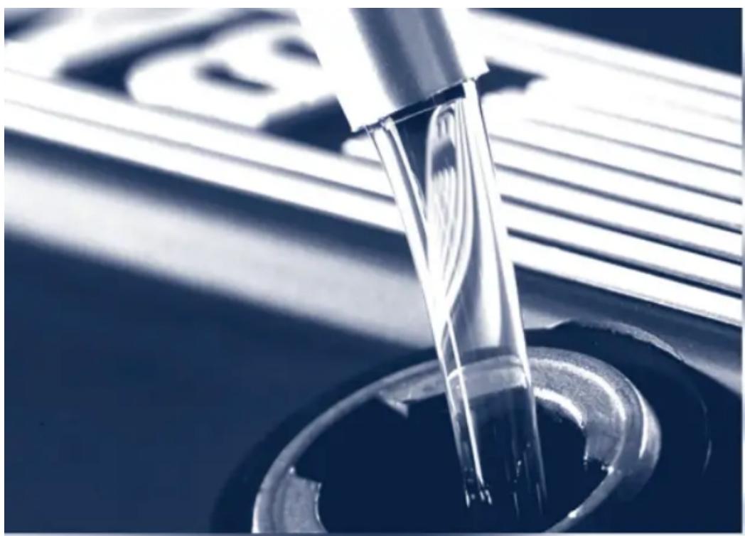 Close-up of a glass pipette dispensing liquid into a circular container (no visible text or symbols)