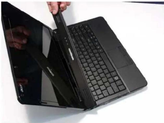 Close-up of a hand inserting a black cable into a black laptop keyboard. No visible text or symbols.