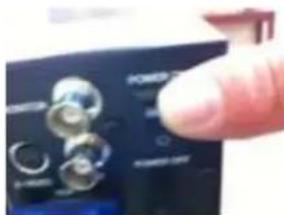 Close-up of a hand pointing to a black electronic device with labeled buttons and ports, including 'POWER' and 'SIN' labels.