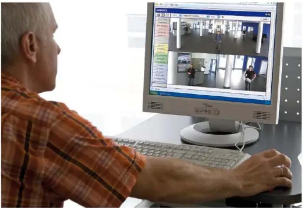 Man using computer in a classroom with video editing interface displaying two scenes of people in a hallway