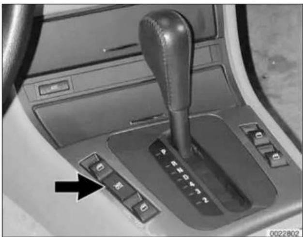 Interior view of a car gear shift control panel with buttons and a black arrow pointing to the left side (no text or symbols visible)