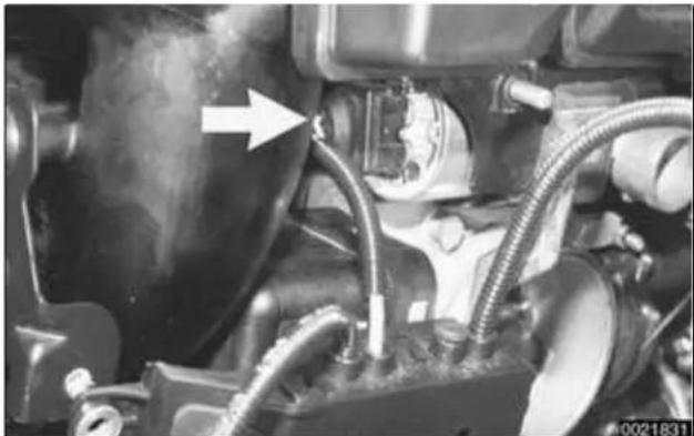 Close-up of an automotive engine component with hoses and a white arrow pointing to a valve (no visible text or symbols)