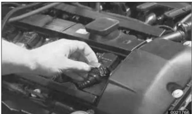 Close-up of a hand adjusting a car engine compartment with visible wiring and components.