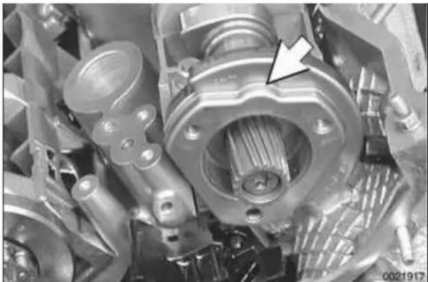 Close-up mechanical assembly showing internal gears and shafts with a white arrow pointing to a specific component (no text or symbols visible)