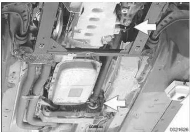Close-up of an automotive chassis frame with visible structural components and two white arrows indicating specific parts. No text or symbols present.