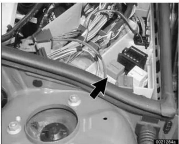 Close-up of an automotive engine compartment with visible wiring and a black arrow pointing to a component (no text or symbols)