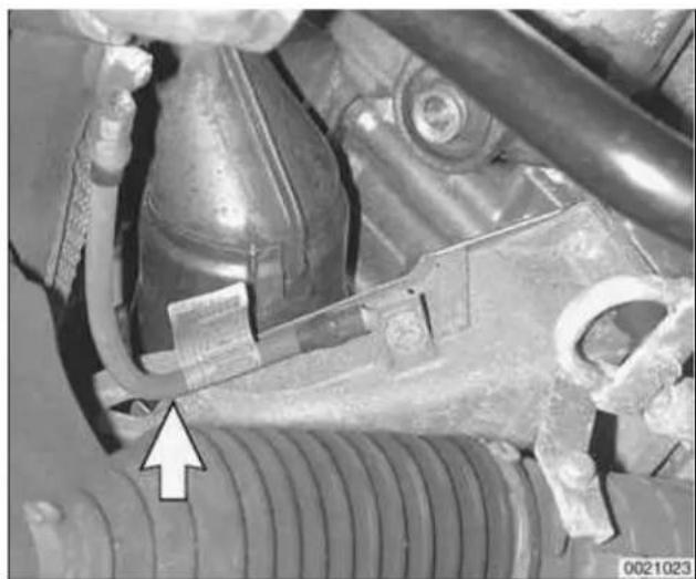 Close-up mechanical assembly showing hoses and components with a white arrow pointing to a specific part (no visible text or symbols).