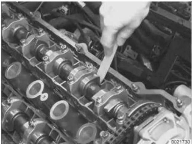 Close-up of hands working on an engine cylinder head with a tool inserted (no visible text or symbols)