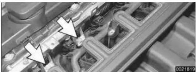 Close-up of an automotive engine bay with visible structural components and two white arrows pointing to a component (no text or symbols)