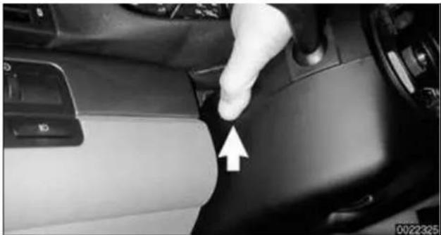 Close-up of a car interior showing a hand pressing down the side of the seatbelt, with a white arrow pointing to the left side (no text or symbols visible)